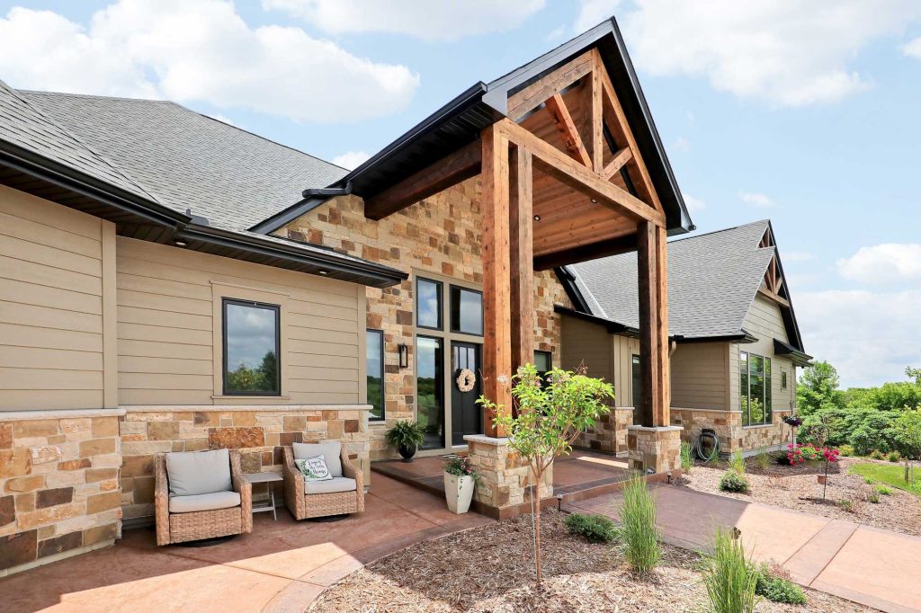 The side view of a new house with a brick front entrance and new landscaping and shrubs and some patio furniture.