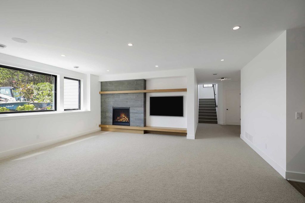 A lower level den with tan carpet, white walls and a built in fireplace and a big screen TV next to it. 3761 William Way Independence Mn 55359 96