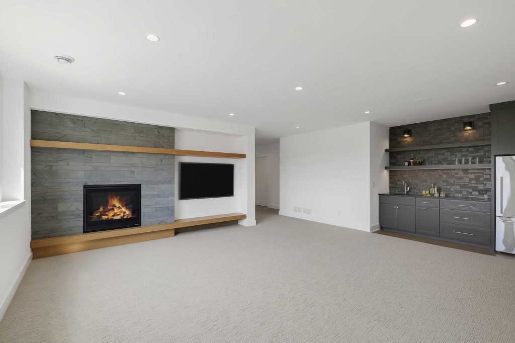 A lower level den with tan carpet, white walls and a built in fireplace and a big screen TV next to it also showing a built in bar. 3761 William Way Independence Mn 55359 97